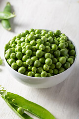 Bowl with fresh peas on a wooden background. Green peas in white bowl.