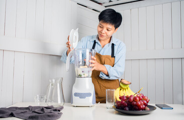 Enjoying Asian man preparing to Make a Smoothie with Swiss Chard, banana, and red grape at a white kitchen home. people are taking care of themselves.