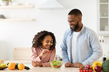 Cheerful african father and daughter cooking healthy salad