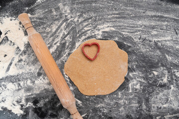 Wooden rolling pin and dough with heart-shaped print. Baking with love. Biscuit making process