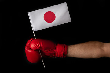 Boxer hand holds flag of Japan. Boxing glove with the Japanese flag. Black background.