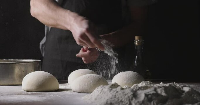 Chef prepares dough for traditional Italian pizza. Cooker sprinkles flour on dough in kitchen, 4k footage