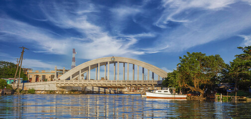 Beautiful shot of the San Juan Bridge under a blue cloudy sky above river with boat and trees