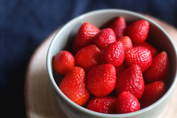 Bowl of fresh strawberries on wooden tray. Selective focus, dark textile background.