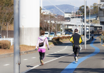Rear view of a man and a woman running on the sidewalk