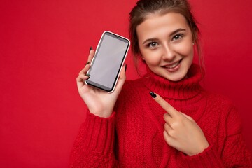 close up Photo of beautiful smiling young woman good looking wearing casual stylish outfit standing isolated on background with copy space holding smartphone showing phone in hand with empty screen
