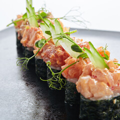 Gunkan Sushi - Gunkan Maki Sushi with Seafood and Spicy Sauce. Sushi with Rice inside and wrapped nori seaweed around. Delicious Gunkan Sushi on black slate plate. Isolated on white background.