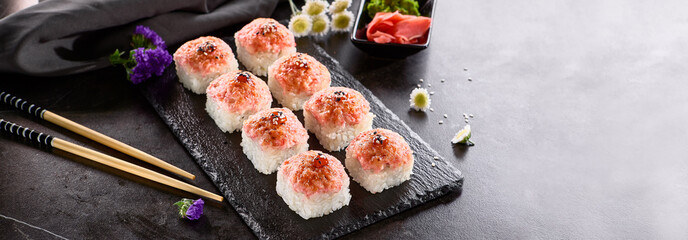 International maki sushi roll on black slate plate. Served with wooden chopstick, green wasabi and pickled ginger. Japanese set with maki sushi roll on dark stone background..