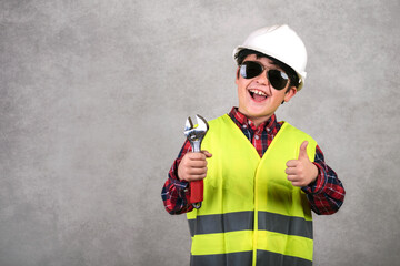 kid construction worker in white helmet and sunglasses and holding a wrench