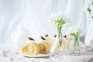 Fototapeta na wymiar Banana Swiss Roll Cake with banana cream filling set on white cafe table.