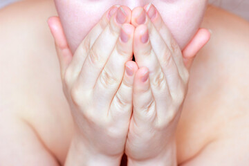 Young caucasian woman covers her mouth and face with hands.