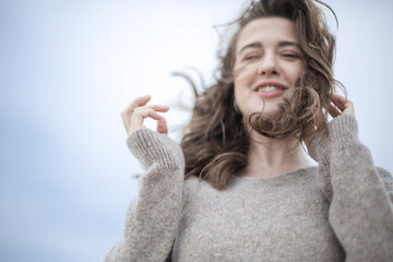 portrait of a beautiful sensual young woman, hair develops the wind, brunette with emotions, hands hair and face, seaside wind outside