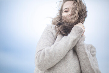 portrait of a beautiful sensual young woman, hair develops the wind, brunette with emotions, hands hair and face, seaside wind outside