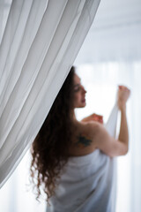 unsharp woman silhouette next to the window , the curtain in front