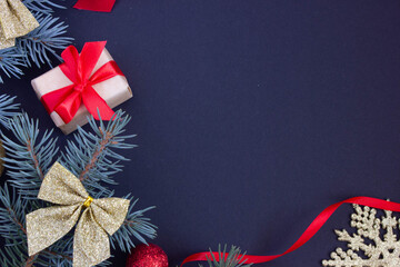 Christmas stylish background with a place for an inscription, Christmas toys and branches of a Christmas tree on a dark background at the edges, a gift with a red ribbon.