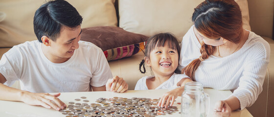 Banner photo of Asian family teach their daughter to saving money and putting coins into glass bank...