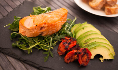 dish of cooked salmon fillet with fresh vegetables and herbs on a black stone plate