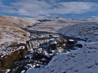 Beautiful view of water cascades of Skógá river near Fimmvörðuháls trail in rocky canyon surrounded by snow-covered meadows on sunny winter day near Skógá village on the southern coast of Iceland.