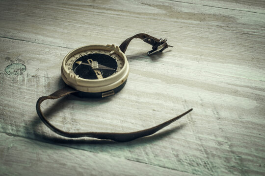 An old wrist compass with a leather strap, lying on a white wooden table