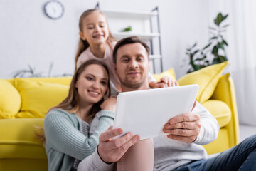 Digital tablet in hands of man on blurred background near family.