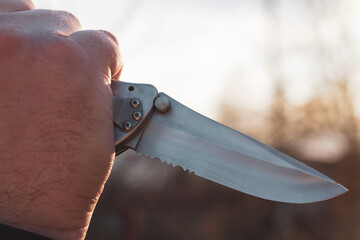 A knife in the hand of a man with a sharp steel blade in the park as a weapon or a means of...