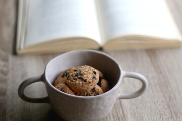 Bowl of chocolate chip cookies and open book on a table. Selective focus.