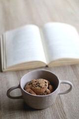 Bowl of chocolate chip cookies and open book on a table. Selective focus.