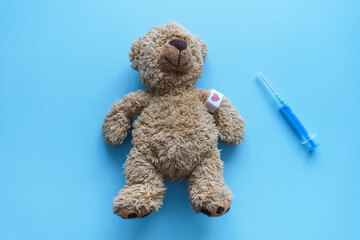 Kleiner brauner Teddybär mit einem Heftpflaster am Arm und eine Spritze auf einem blauen...