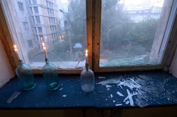 Three candles burning in glass jars placed on a windowsill, broken glass near