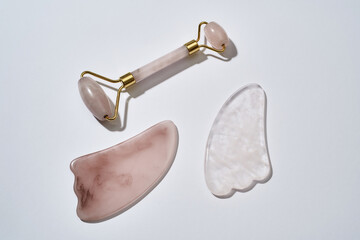 Rose quartz facial massage tools, face roller and Gua Sha scrapers isolated on light background