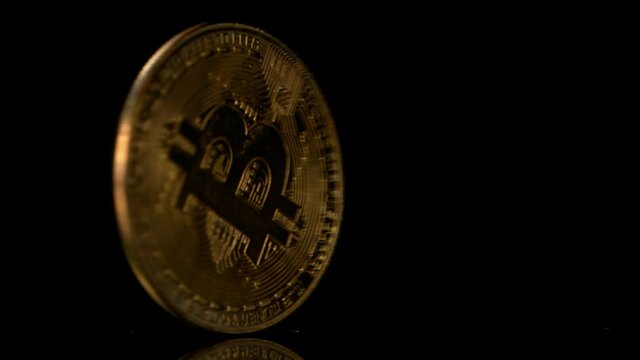 Close up one golden bitcoin physical coin spins over black background, super slow motion