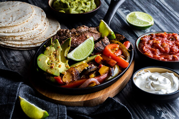 Close up of a skillet filled with steak, peppers and avocados to make fajitas, surrounded by other...