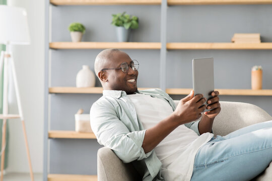African american man reading e-book on digital tablet or browsing internet, enjoying weekend and resting on armchair
