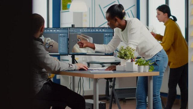 Professional heavy industry team of engineers working on computer with two monitors using CAD software with integrated development environment to design industrial machinery component.