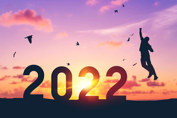 Silhouette man jumping and birds flying on sunset sky at top of mountain and number like 2022 abstract background. Happy new year and holiday celebration concept. Vintage tone filter color style.
