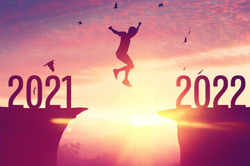 Silhouette man jumping and birds flying between cliff with number 2021 to 2022 at top of mountain...