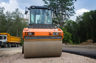 large orange roller on road paving works. In the background is a dump truck. Improvement of the city. Equipment for road construction and repair