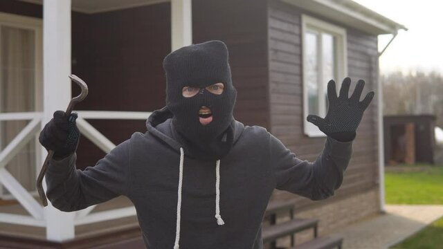 Portrait of angry burglar in black balaclava and gloves threatens