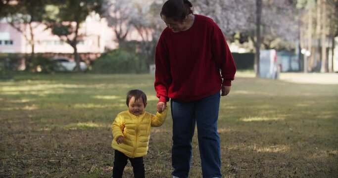 Asian baby girl walking in the spring field with her mother outdoor young woman holding her daughter hand relax in the garden