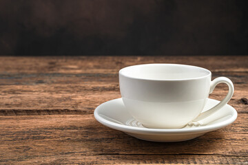 An empty white ceramic cup and saucer on a wooden brown background.
