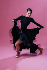Beautiful woman wearing a  black dress posing against pink background in studio. 