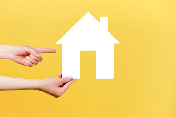 Fototapeta na wymiar Close up of female hand raising and pointing to white paper house, isolated over pastel yellow studio background wall with copy space for advertisement. Property and mortgage concept