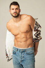 Muscle strong beautiful stripped male model shirtless in denim jeans and etno jacket on grayisolated font background