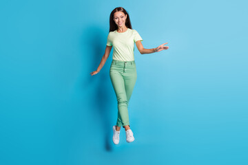 Fototapeta na wymiar Full length photo of funny adorable young lady wear green clothes jumping high isolated blue color background