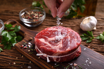 Hand sprinkling salt on fresh raw beef meat on a cutting board