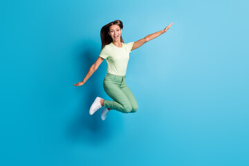 Fototapeta na wymiar Full length photo of charming sweet young woman wear green outfit jumping arms sides isolated blue color background