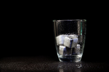 stainless steel cubes simulating ice in whisky glass on a black table.