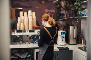 Focused woman in barista uniform making coffee for customers - obrazy, fototapety, plakaty