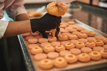 Skillful cook puttinf filling onto macarons with a confectioner syringe