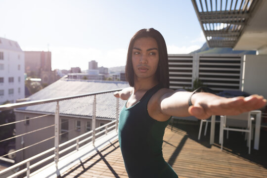 Mixed race transgender woman practicing yoga standing on roof terrace in the sun